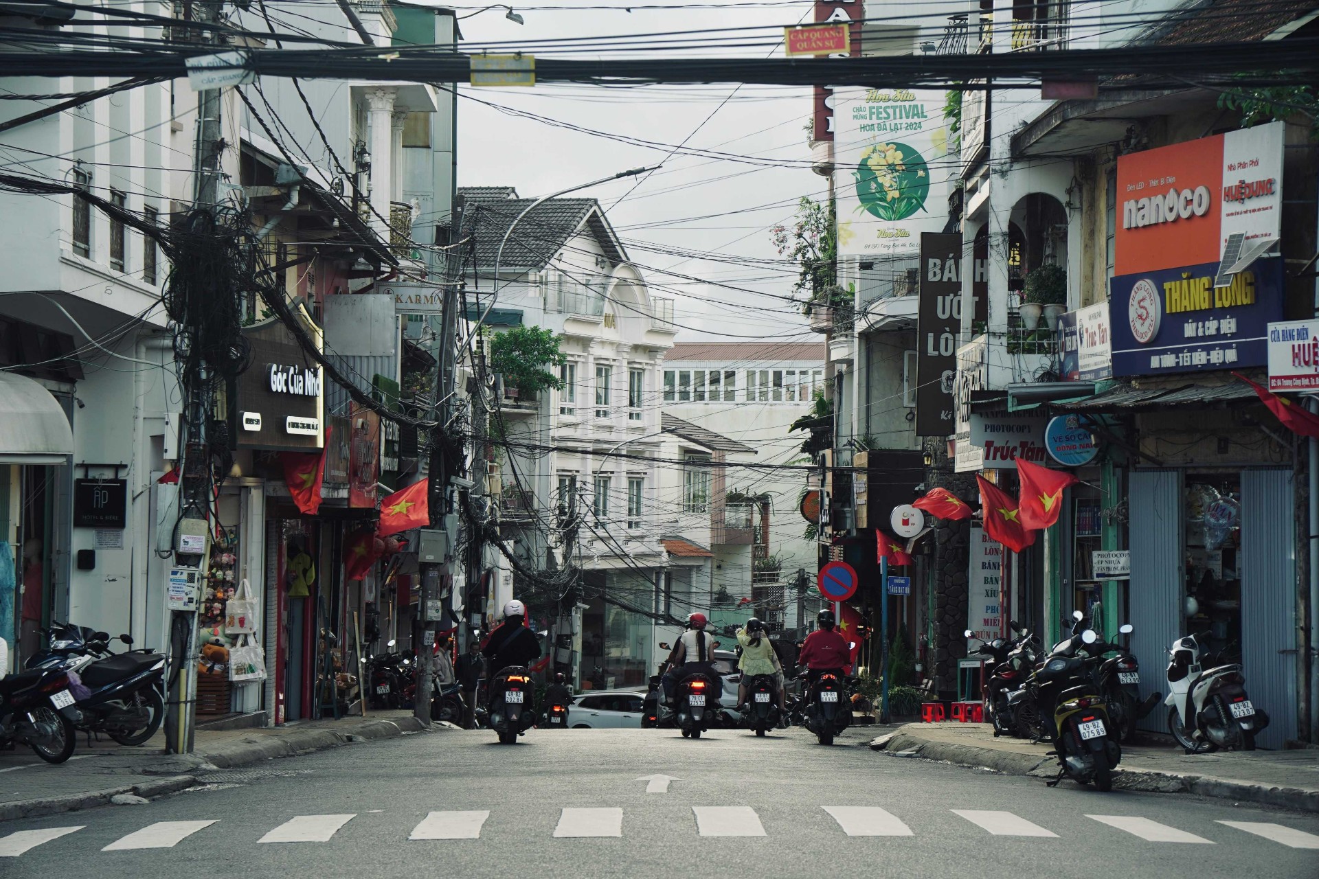 Motorbikes and shopfronts on a busy Vietnamese street lined with red flags and tangled power lines