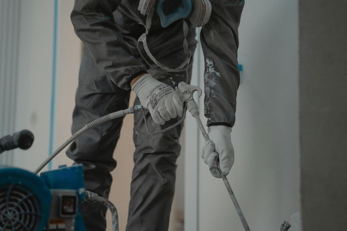 Industrial painter in protective gear using spray equipment on a construction site