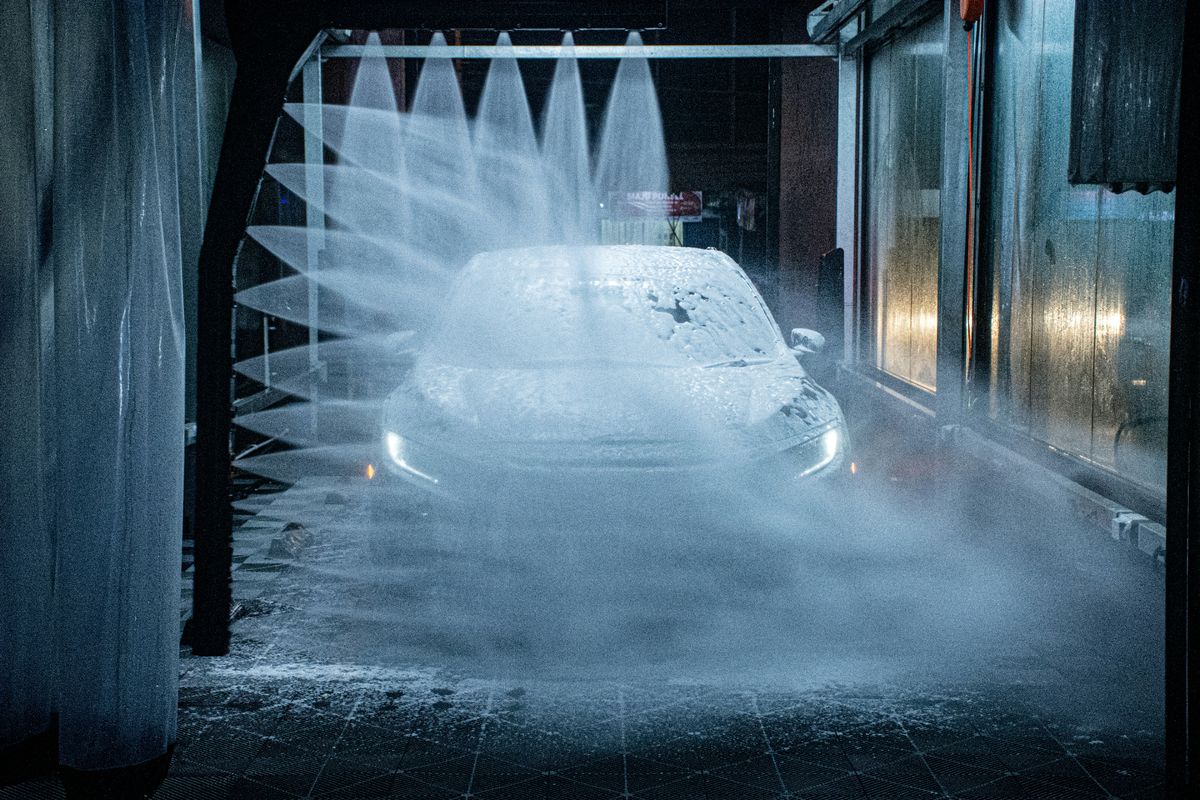 Car passing through an automated car wash with high-pressure water jets spraying from both sides