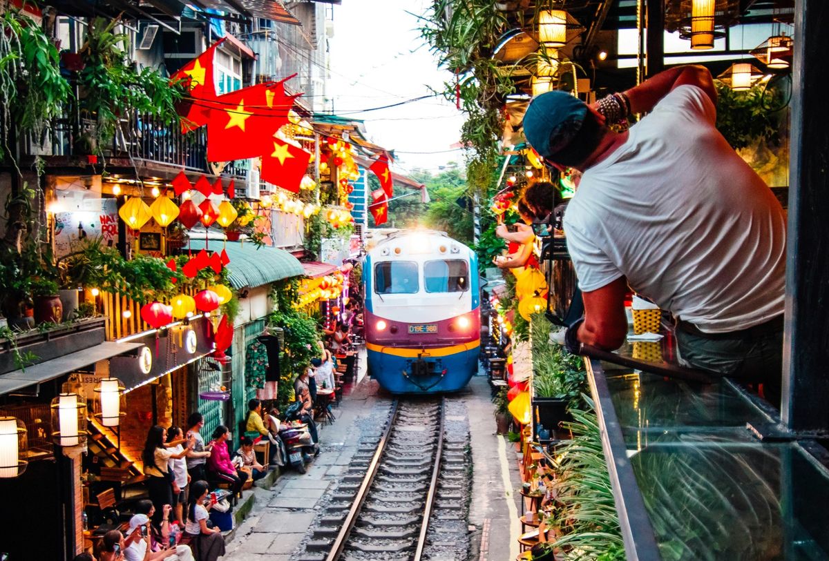Train passing through narrow Hanoi street lined with lanterns, flags, and cafe seating